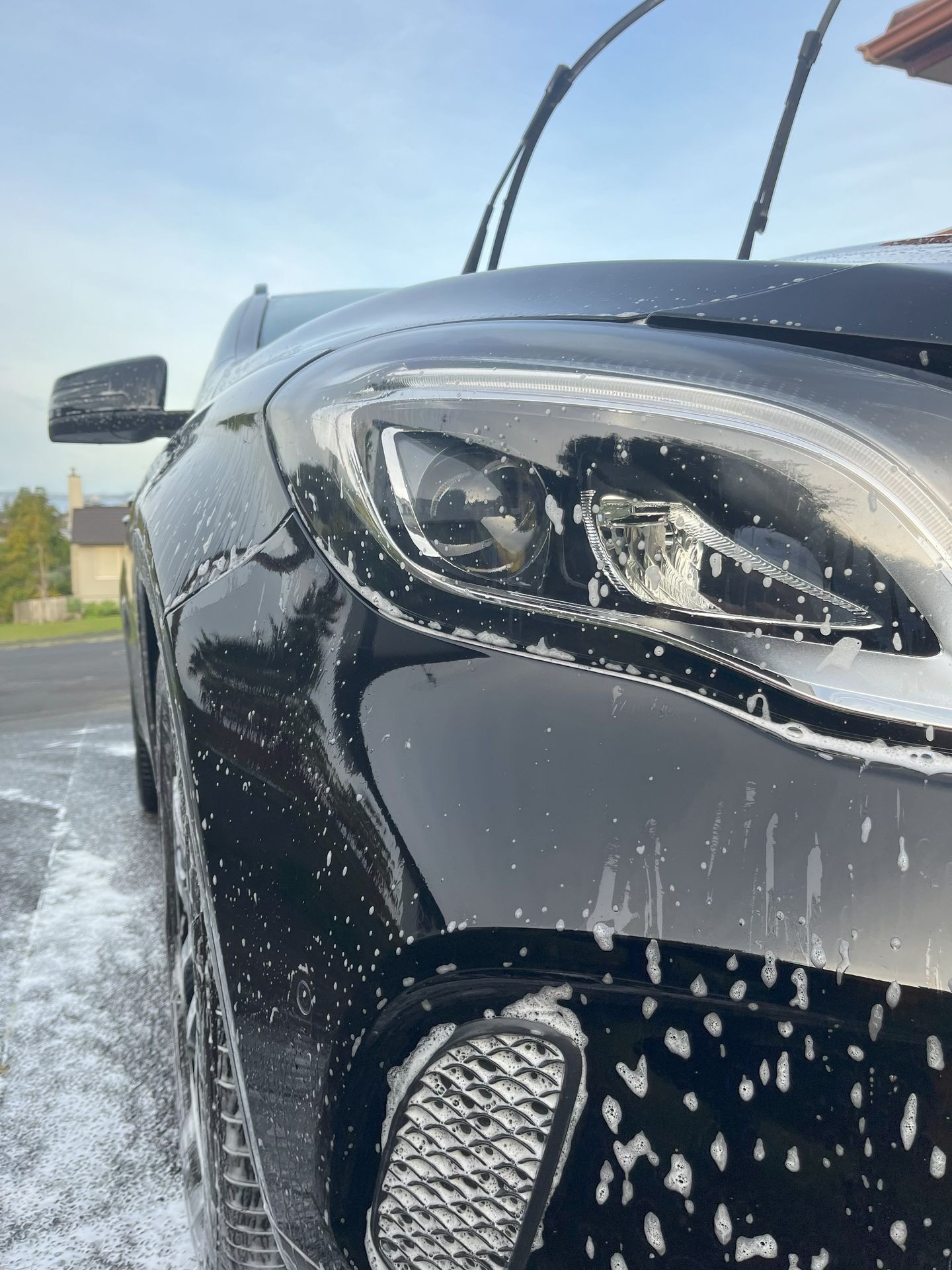 Close-up of a black car being washed with soap suds on the headlight and body.