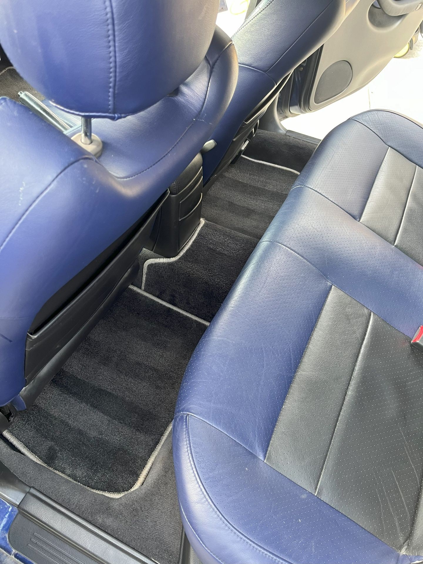 Back seat view of a car with blue and black leather upholstery and dark carpeted floor mats.