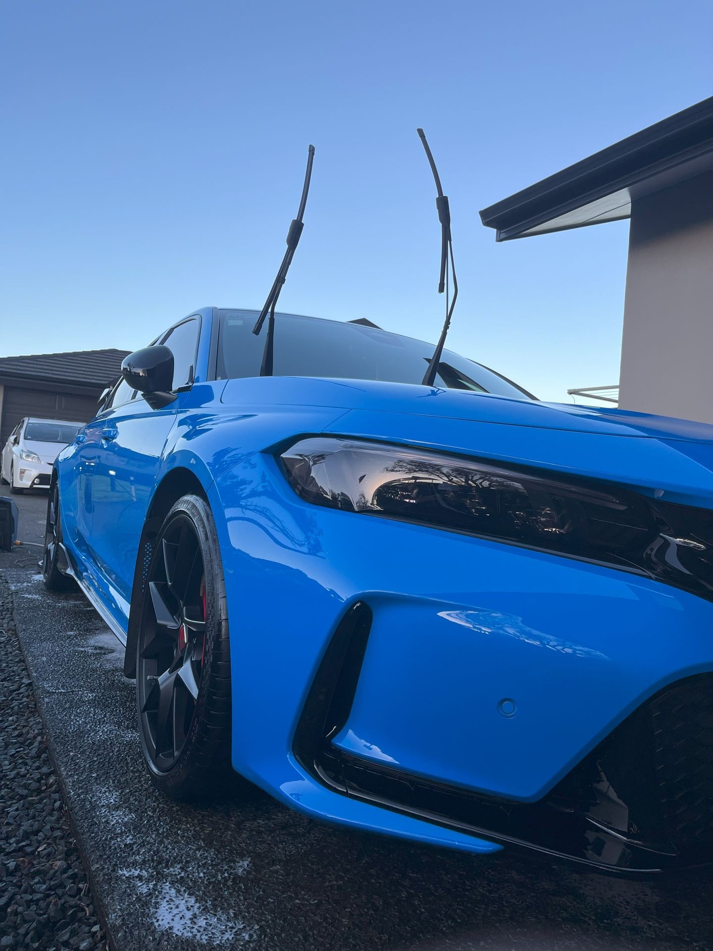 Close-up of a blue car with raised windshield wipers, parked on a driveway.